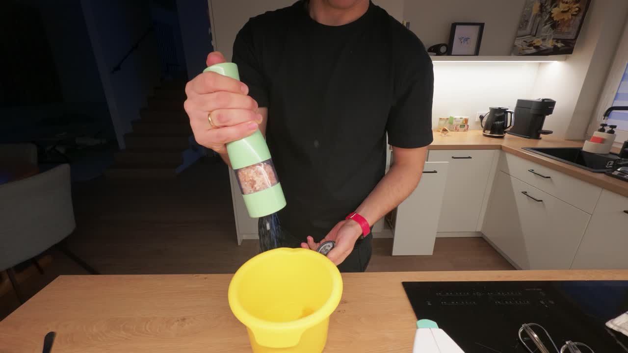 Persona ordenando activamente en una cocina contemporánea con líneas limpias y una iluminación cálida. Centrada en organizar con un cubo amarillo brillante y electrodomésticos elegantes. Plano medio.