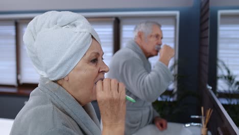 Pareja-Mayor,-Abuela-Y-Abuelo,-Cepillándose-Los-Dientes-Y-Mirándose-En-Un-Espejo-En-El-Baño