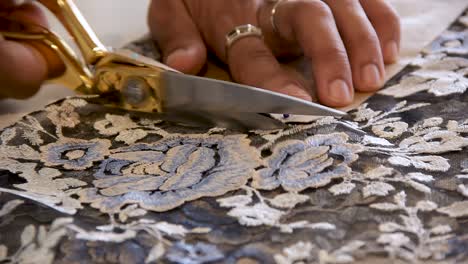 close up of dreesmaker cutting a flower shaped fabric with a sewing pattern attached with colorful pins with a golden handle scissors - interior shot handheld