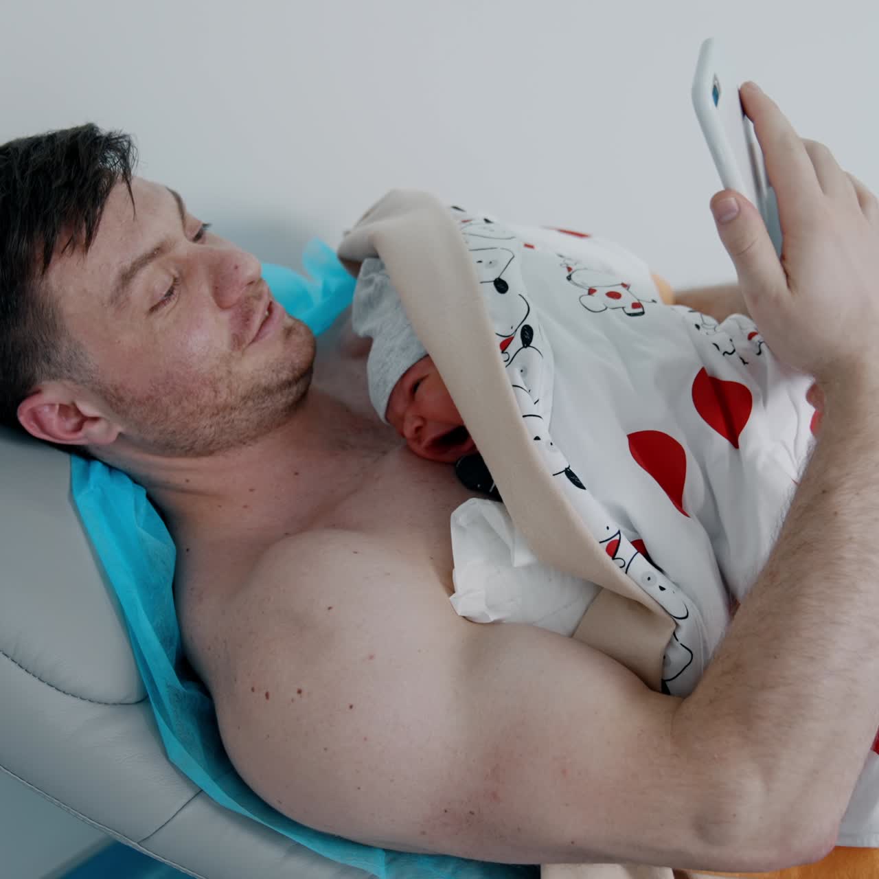 Caucasian bearded male takes selfie of himself and of a child lying on the chest. Newborn is placed on dad's chest for skin to skin contact