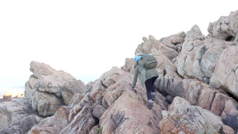 hiking on rocky mountain, woman with backpack and rolled-up mat climbing up, copy space