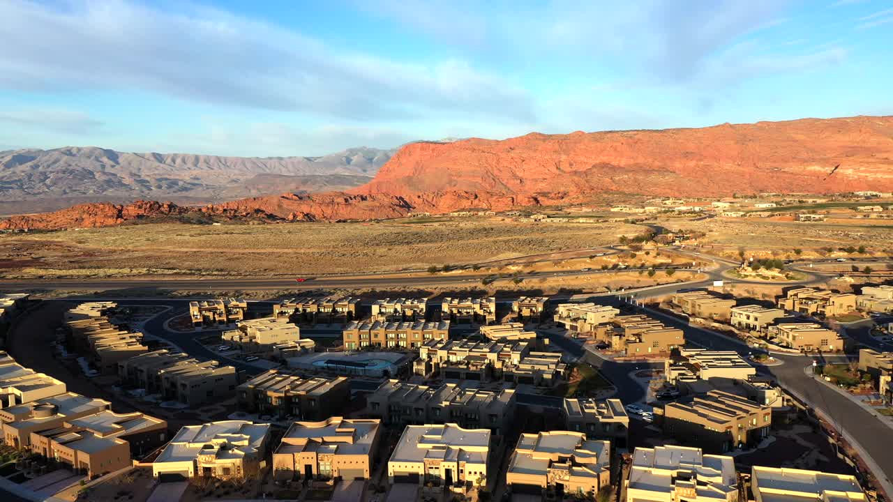 석양에 사막과 산의 도로에서 주택 개발과 지나가는 자동차를 날고 있습니다.