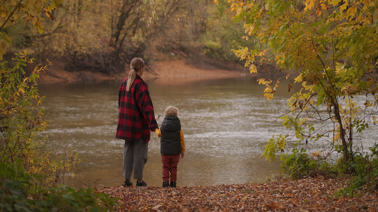 자연에서 어린 아이와 함께 한 여성의 행복과 평온함 사람들이 가을 날에 그림 같은 숲 연못의 연안에 서 있습니다.