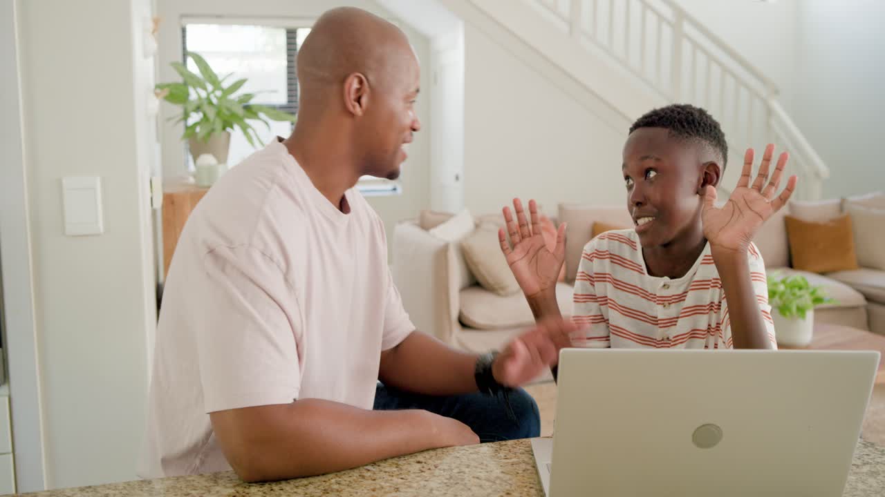 African American father, teen son leaning at counter, father speaking guiding typing task on laptop