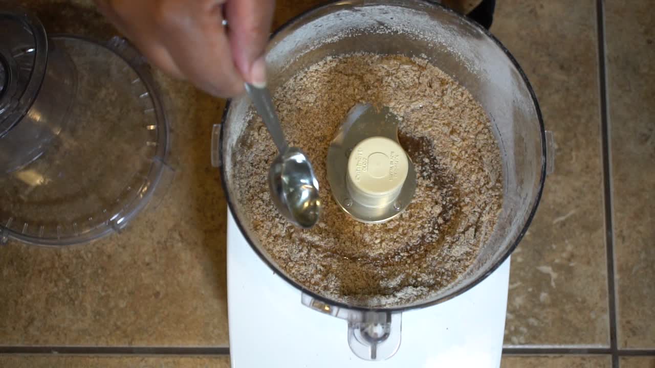 agregando una cucharada de aceite de coco a los ingredientes secos en el procesador de alimentos, a cámara lenta