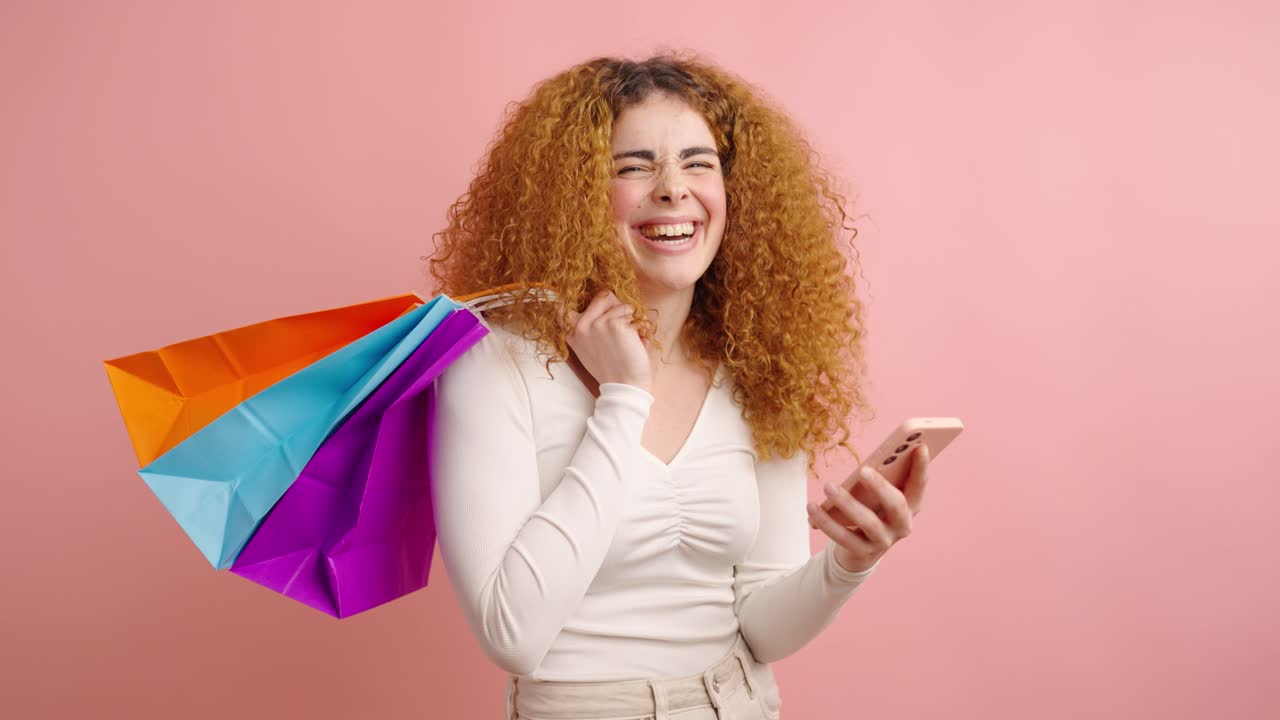 Excited woman with shopping bags and cellphone in studio