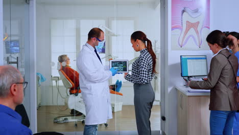 Orthodontist-using-tablet-explaining-dental-x-ray-to-patient