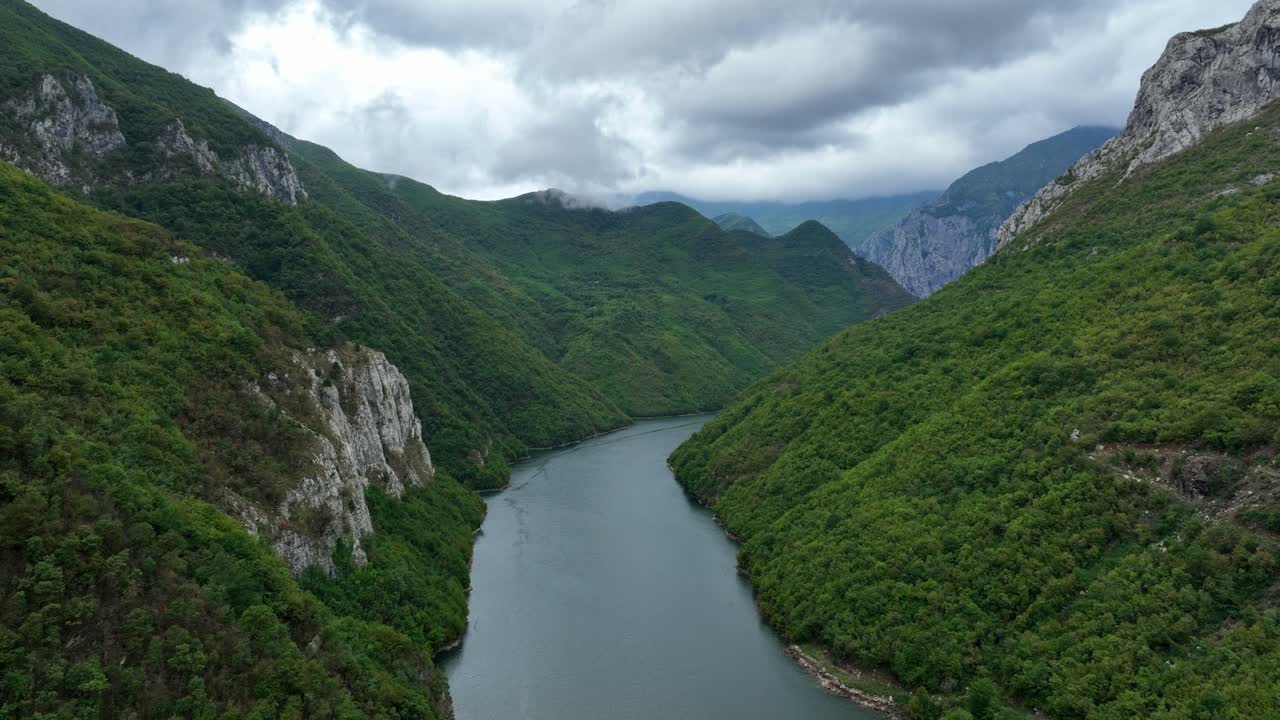 Aerial shot of Lake Komani surrounded by lush green mountains and cloudy skies