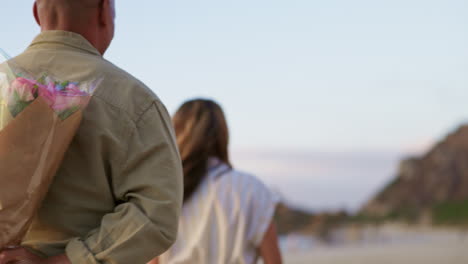 man, woman and surprise with flowers on beach date