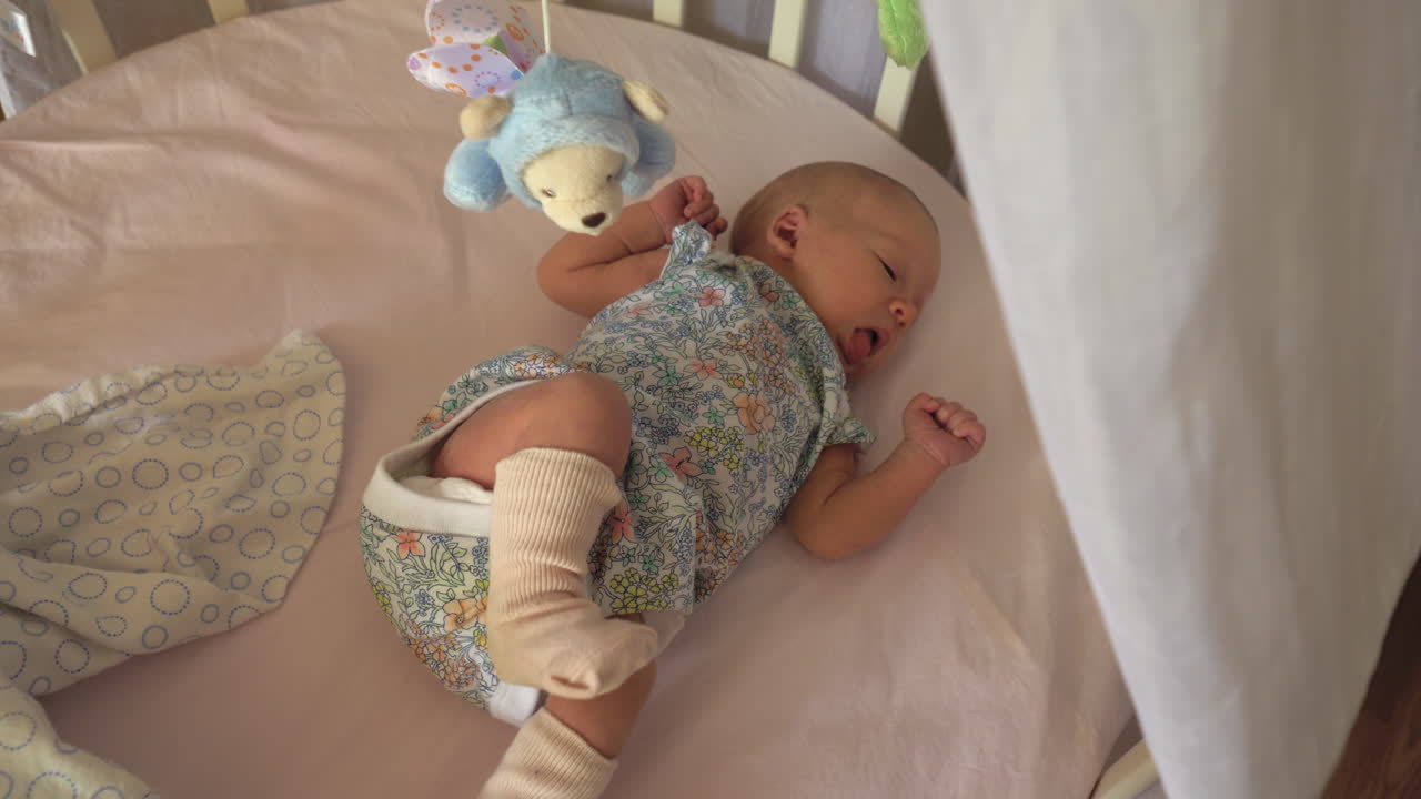 Neonato con il singhiozzo sdraiato nella culla con giostrina