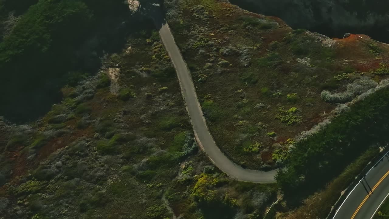 Cars drive along a winding road near the coast in California, USA