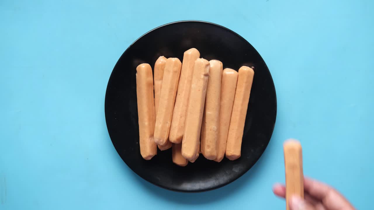 mano sosteniendo una salchicha de un plato