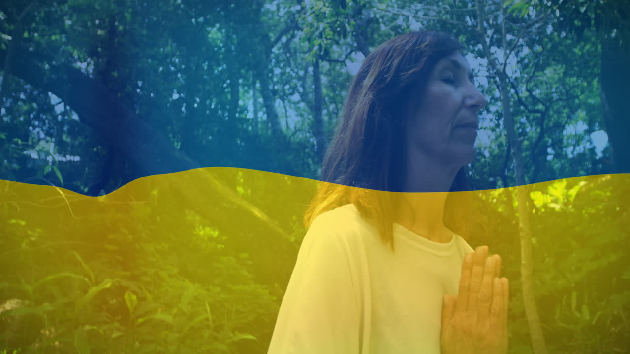 Animazione della bandiera dell'Ucraina su donna caucasica che prega all'aperto