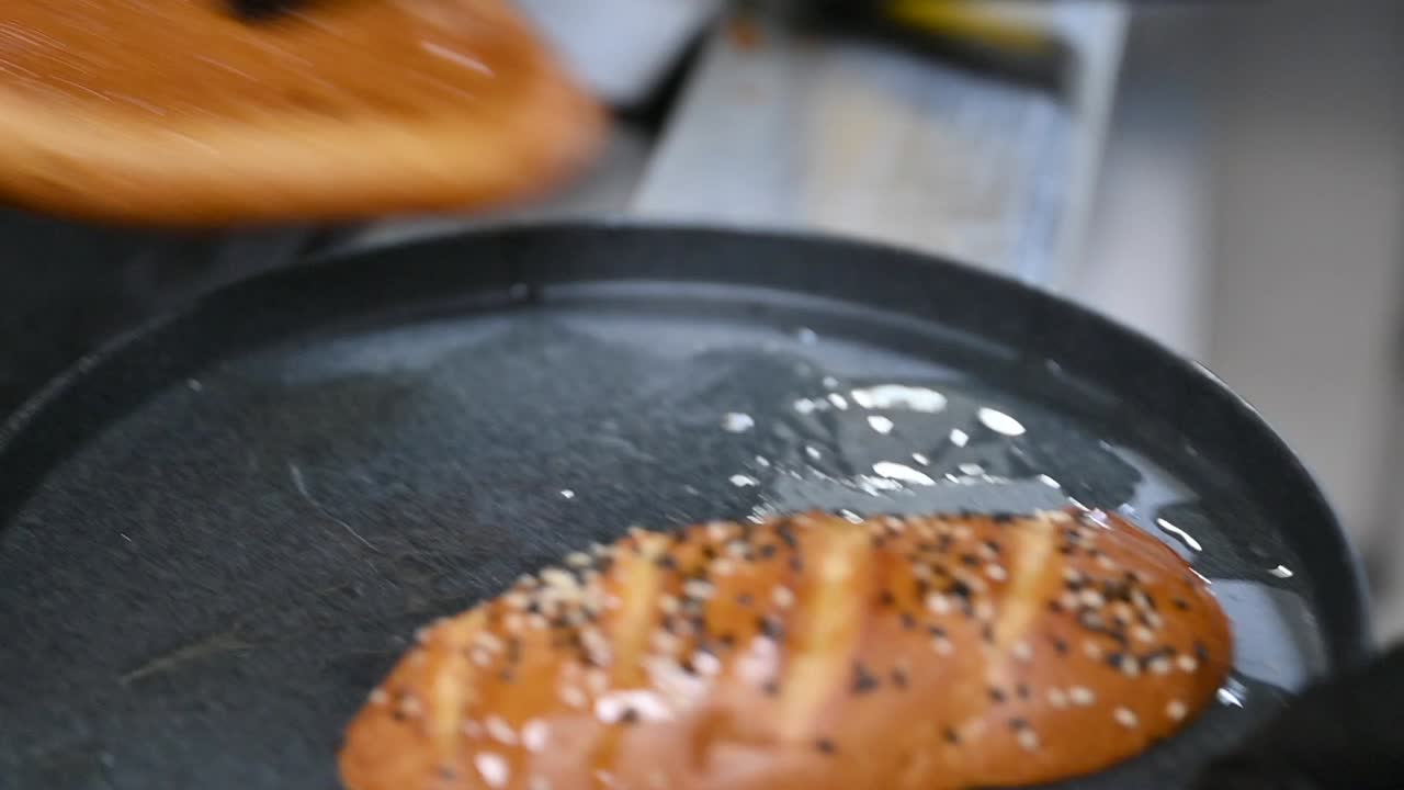 pan de hamburguesa siendo tostado en aceite caliente en un restaurante