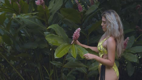 chica de cabello rubio juega con una flor de chaconia en un sexy bikini tanga