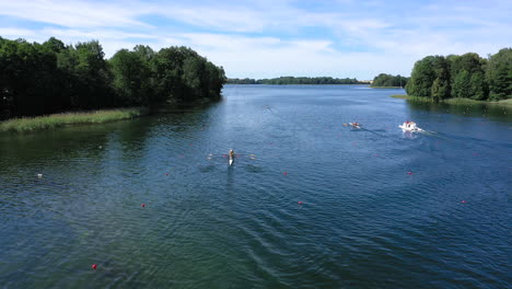 aerial: kayaking athletes in paddling canoes on the surface of the lake racing on the buoy marked lines against coach sailing boat