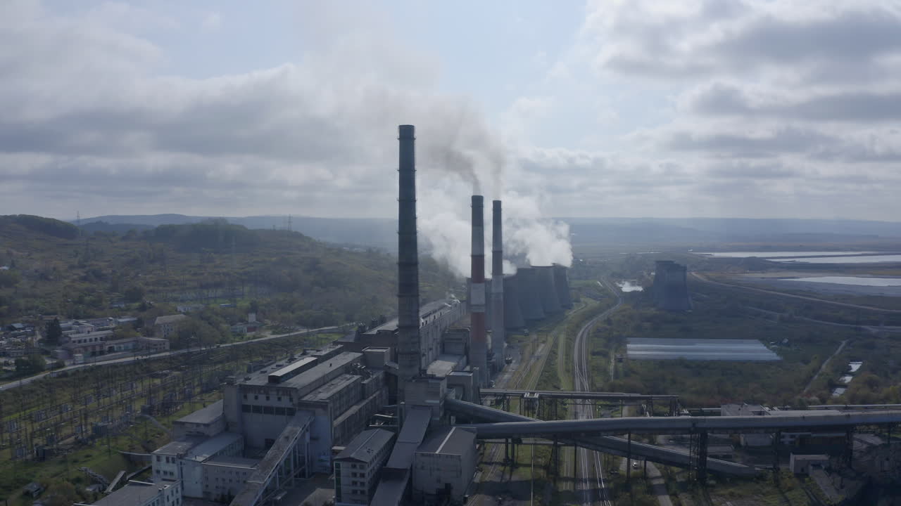 Ripresa panoramica lenta di una centrale elettrica a carbone con le sue ciminiere che rilasciano fumo bianco e grigio nell'aria in una giornata soleggiata e nuvolosa