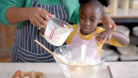 happy african american mother and daughter preparing dough in bowl in kitchen, slow motion