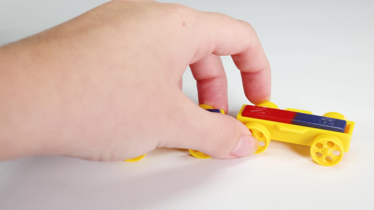 Hands manipulate magnetic toy cars on a white surface, illustrating magnetic attraction and repulsion with colorful components