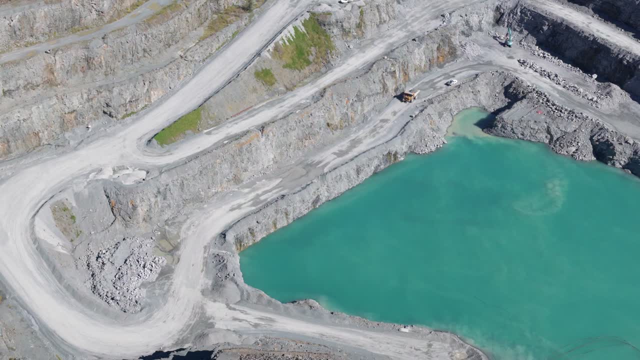 Aerial footage of a quarry with vibrant turquoise water, showcasing terraced rock formations and industrial activity under bright daylight