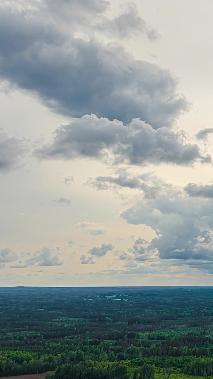 Aerial vertical timelapse of dramatic moving clouds drifting across cloudy sky above vast green forests stretching to flat horizon in rural Latvia at dusk