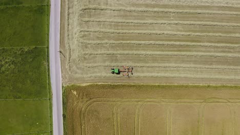 Harvesting-tractor-with-its-twin-rotor-rake-trailer-filmed-from-above-working-at-a-field,-collecting-the-wheat-in-straight-rows-to-optimze-the-harvest-workflow