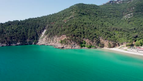 rotating aerial reveal of paradise beach with turquoise water, surrounded by green vegetation and high mountain peaks, thassos island, greece, europe