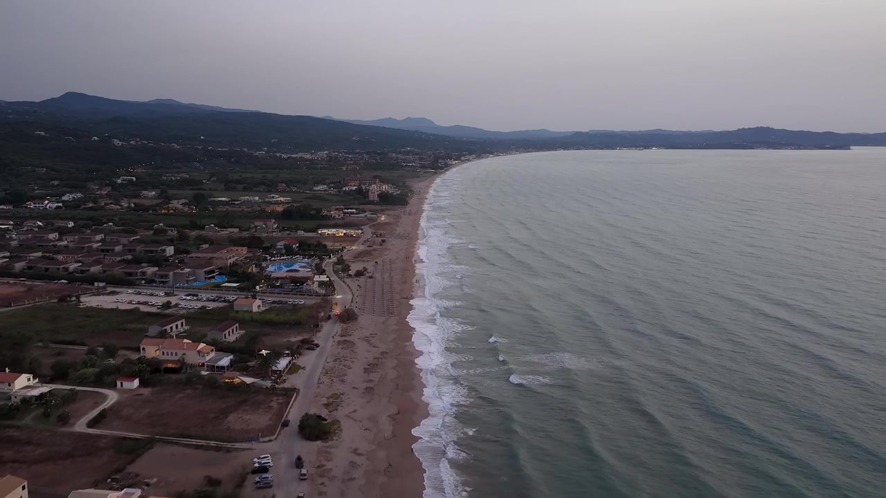 Volo aereo sopra Almyros fino alla spiaggia di Acharavi, Corfù settentrionale, Grecia, al tramonto, che mostra località balneari e il tranquillo Mar Ionio