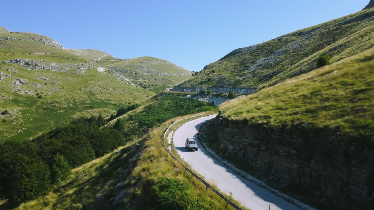toma aérea de un coche todoterreno que viaja por carreteras estrechas debajo del pico de la montaña
