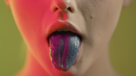 cerca de la boca de la chica masticando y soplando chicle con lengua de color azul, toma de estudio con iluminación colorida
