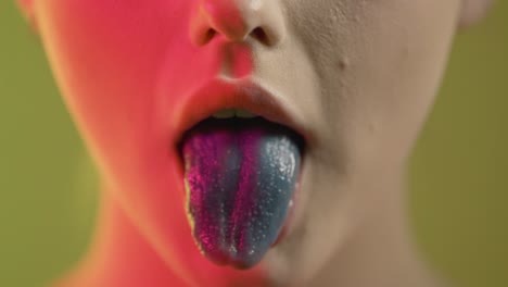 close up of girl's mouth chewing and blowing bubble gum with blue colored tongue, studio shot with colorful lighting