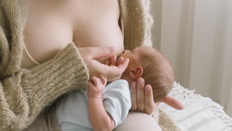 close up an unrecognizable mother breastfeeding her newborn baby while sitting on the bed at home