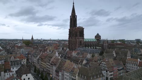 expansive aerial view of strasbourg’s skyline with the majestic notre-dame cathedral at the center, surrounded by traditional tiled rooftops and historic european architecture under a cloudy sky