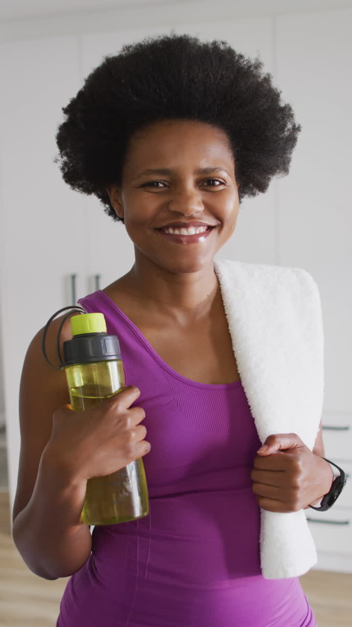 video vertical del retrato de una mujer afroamericana sonriendo y sosteniendo una toalla y una botella de agua