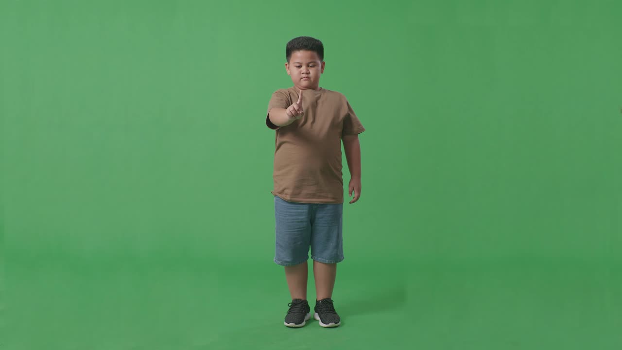 아시안 소년의 몸이 가득 차 있습니다. 스, 한 손가락 제스처, 금기 표지, 스튜디오의 녹색 스크린에 서 있습니다.