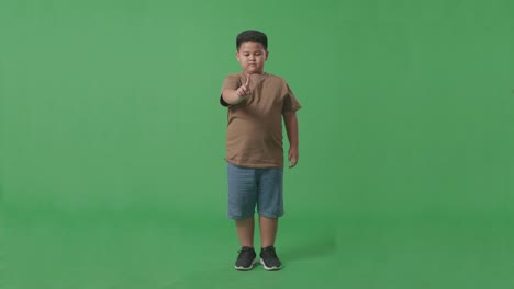 cuerpo lleno de niño asiático mostrando parada, un gesto de dedo, signo tabú, de pie en la pantalla verde en el estudio