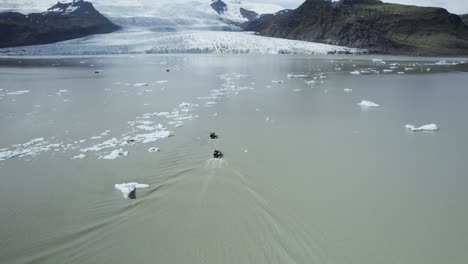 Boote,-Die-Durch-Gletschergewässer-In-Island-Navigieren,-Mit-Einer-Atemberaubenden-Bergkulisse