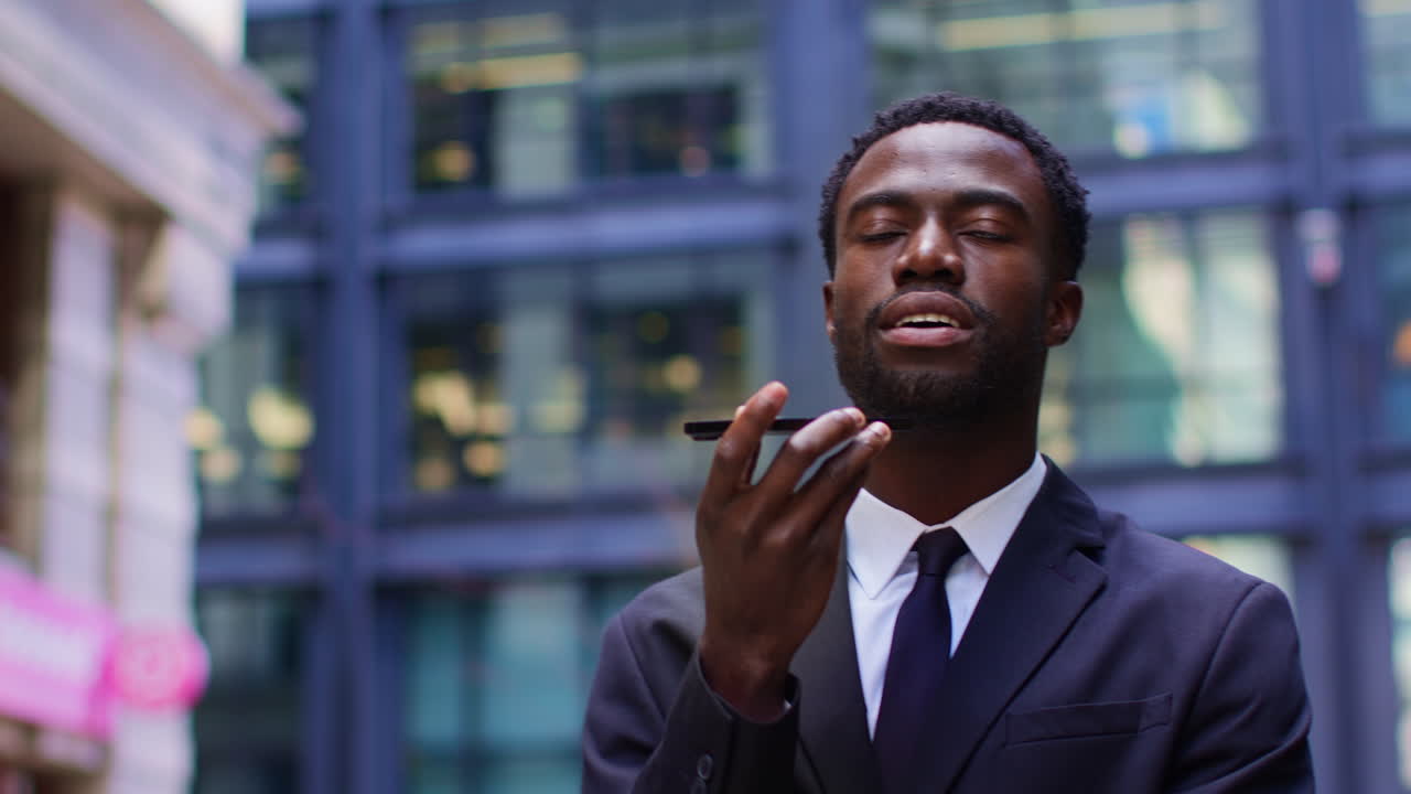 un joven hombre de negocios con traje hablando por teléfono móvil usando un micrófono incorporado de pie fuera de las oficinas en el distrito financiero de la ciudad de londres, reino unido, filmado en tiempo real.