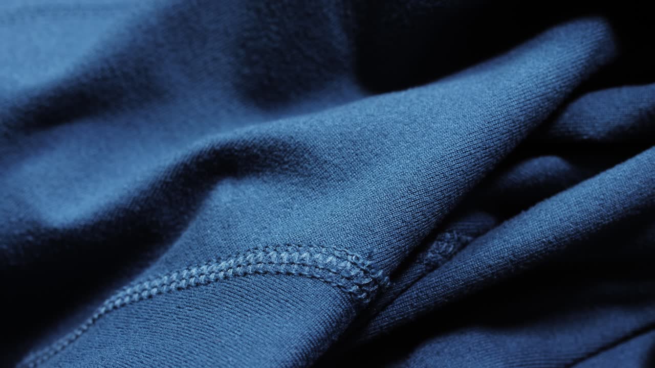 Teal polyester sportswear shows soft folds and a coverstitch seam as the camera pans