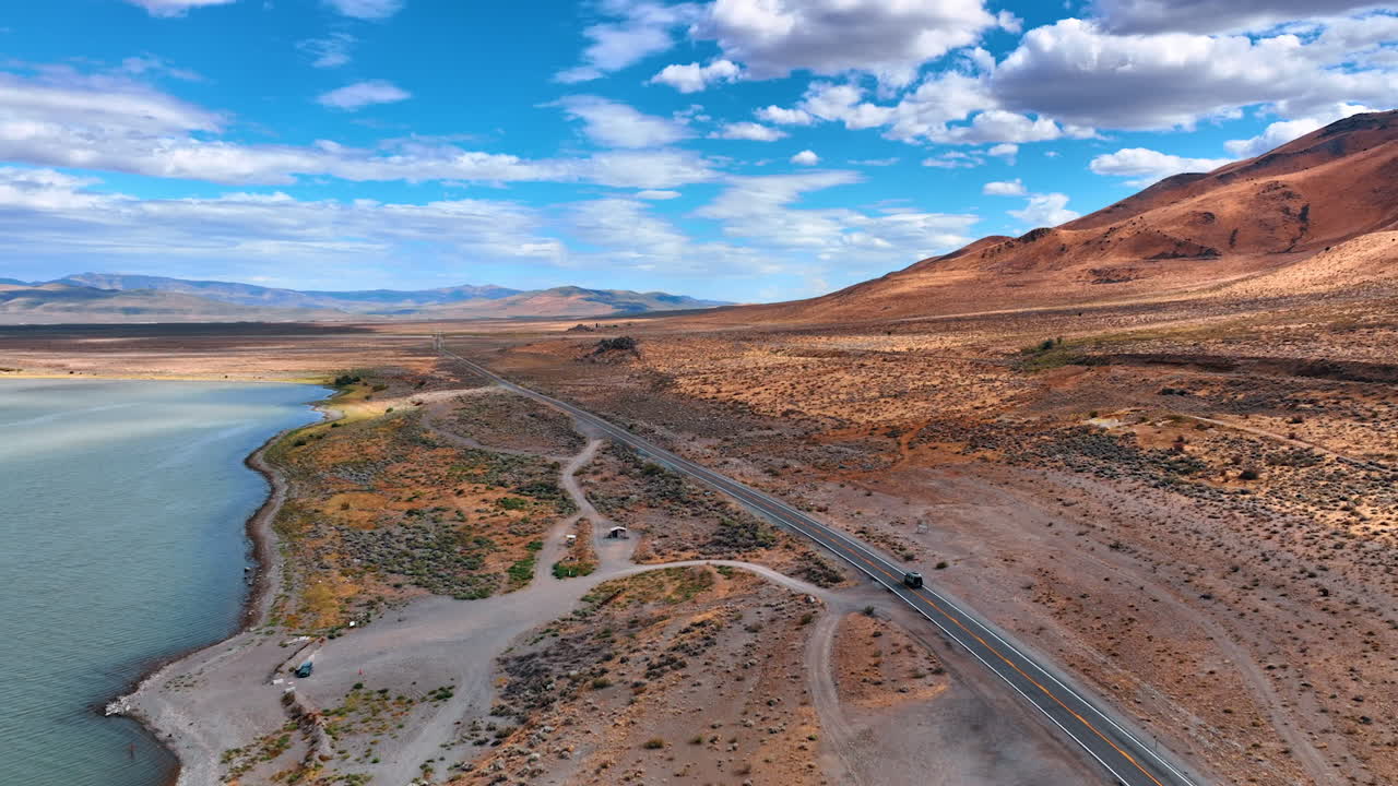 Following the car riding by the highway along the waterscape. Travel by the deserted landscape at daytime. Aerial view