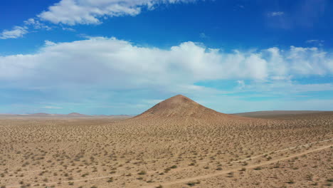 Flying-towards-a-volcanic-cone-shaped-mountain-in-the-middle-of-the-Mojave-Desert's-rugged-terrain