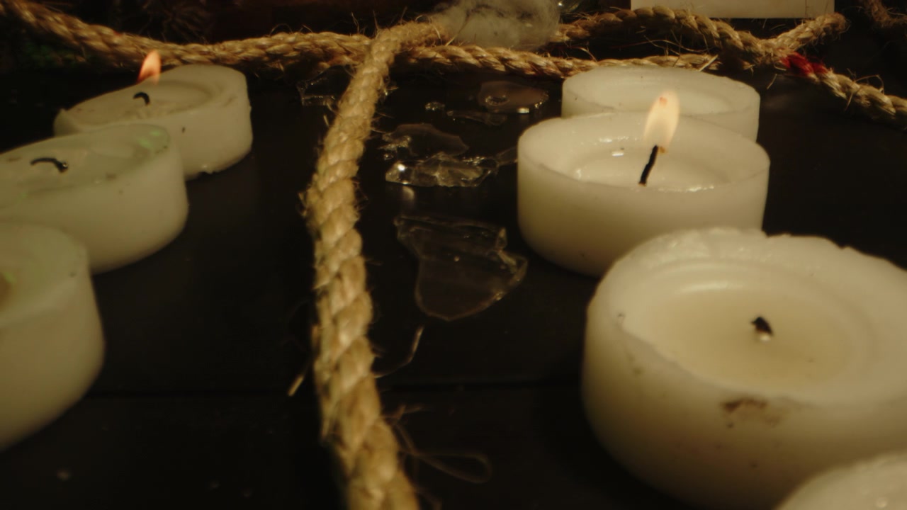 Macro dolly out of a long rope running between burning candles and broken glass at an occult altar