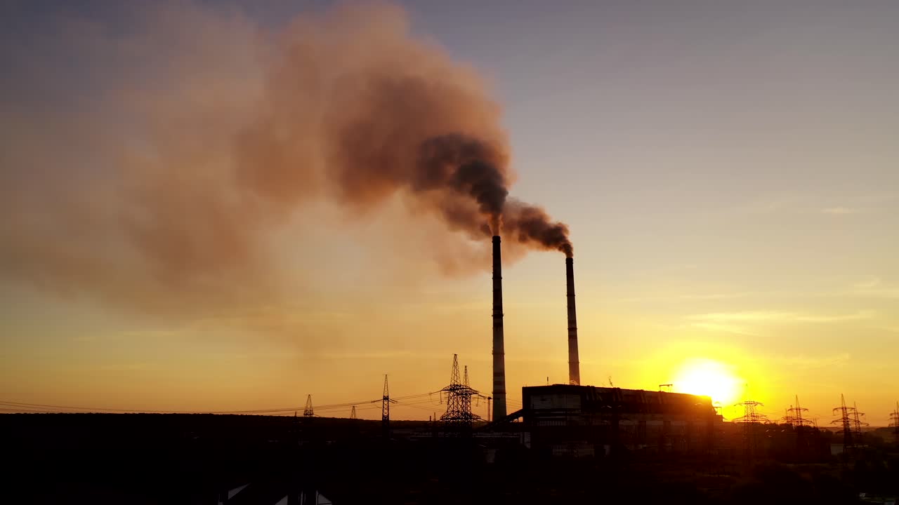 Dark industrial factory in the evening. Metallurgical plant. Smoke coming out of factory pipes at sunset. Drone view. Motion camera back.