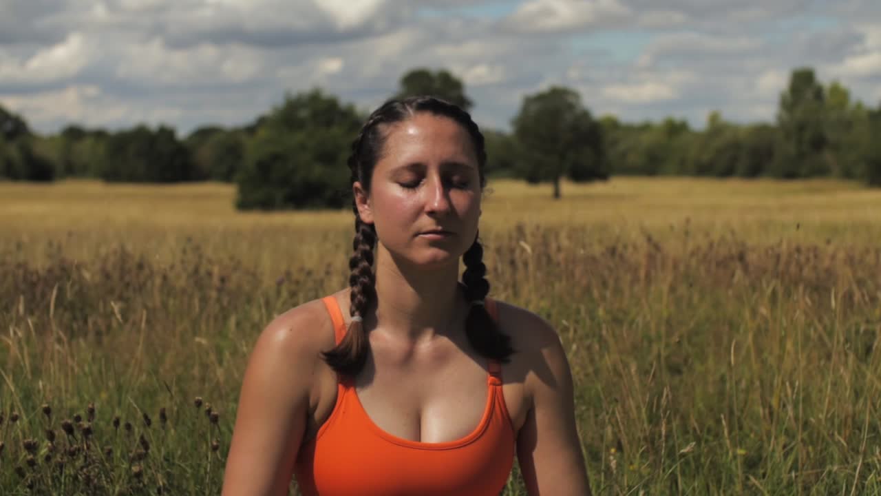 mujer sentada en un campo de hierba larga yoga meditando día soleado reino unido, hertfordshire pan de tiro medio de izquierda a derecha