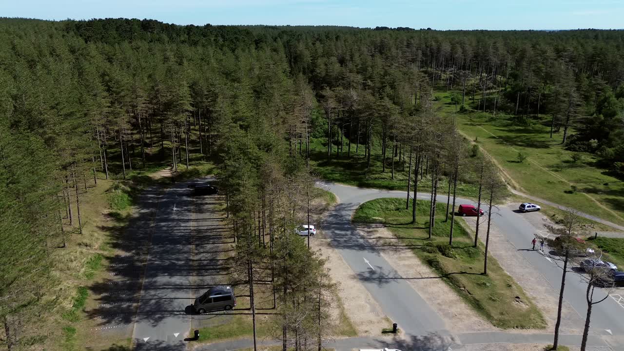 Newborough forest beach car park aerial view flying over sunny woodland pine trees visitors parking