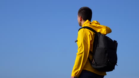 thoughtful backpacker man with yellow raincoat looking at blue sky in windy day