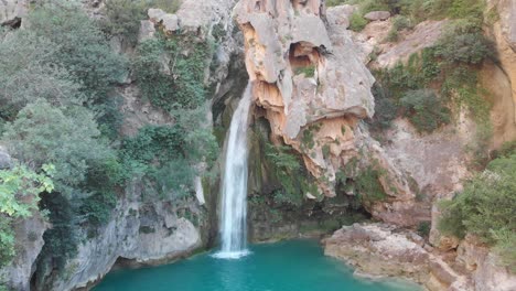 aerial elevating shot over a spectacular waterfall, skull shape rock, as the power of nature formed a clear green lake in the mountains