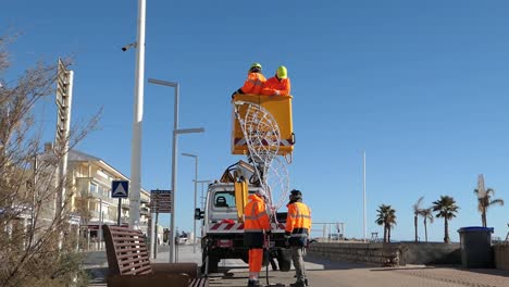 council workers wearing orange clothes putting up christmas lights at valras plage in the south of france on mediterranean coast