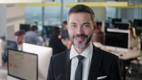 retrato de un hombre de negocios adulto jefe de pie en la oficina sonriendo mirando a la cámara mientras los empleados están ocupados trabajando en el fondo