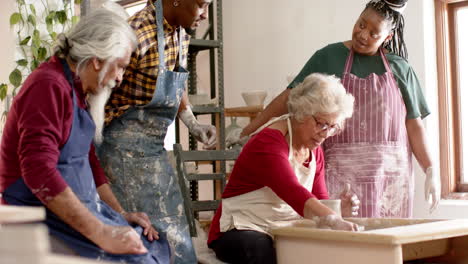 happy biracial female potter with others, using potter's wheel in pottery studio, slow motion